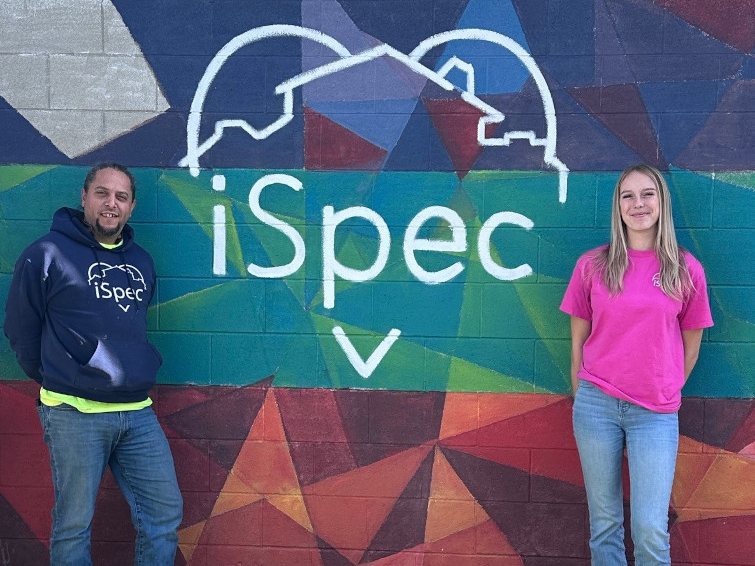 Two members of the iSpec team standing in front of the iSpec heart-and-house mural