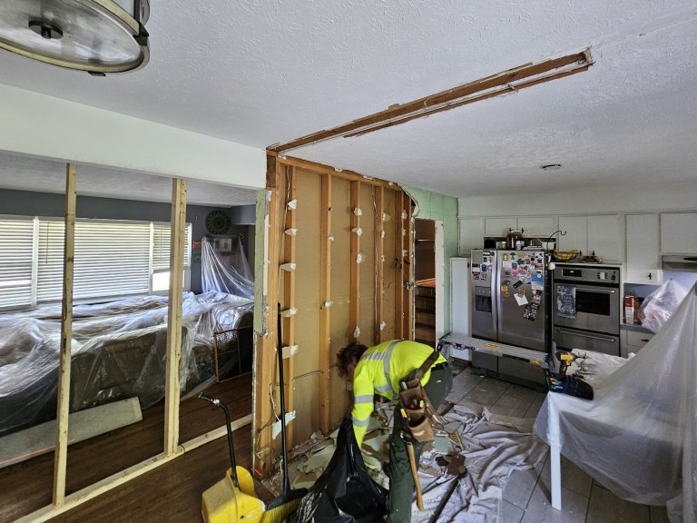 Bearing wall stripped to studs with temporary shoring in place — plastic sheeting protecting the homeowner's furniture and finishes on both sides