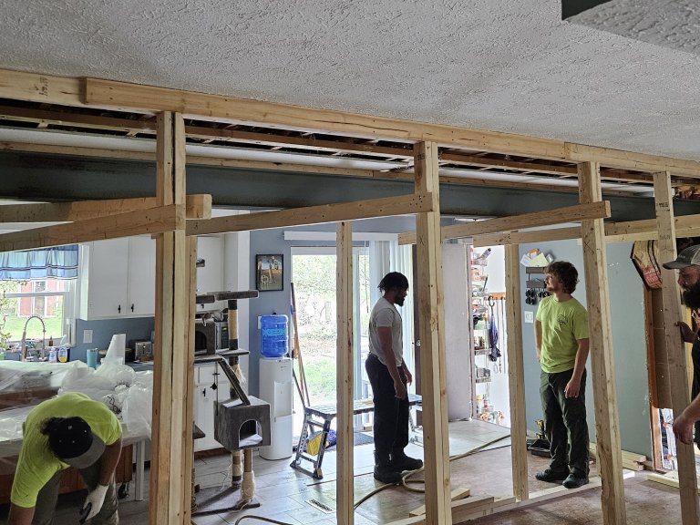 Full crew coordinating the beam install — kitchen visible through the shoring from the living room side
