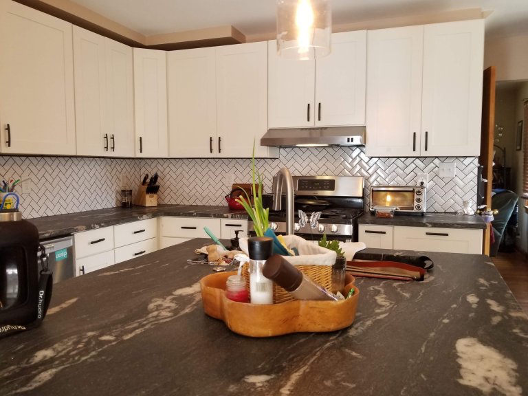 Finished kitchen — custom cabinetry, leathered marble, and herringbone backsplash